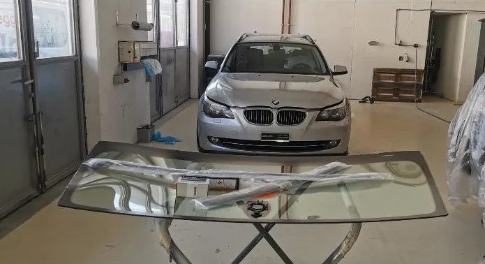 Neue Frontscheibe auf dem Montagebock vor einem BMW
